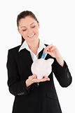 Beautiful woman in suit inserting a money bill in a pink piggy b