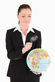 Good looking female in suit holding a globe and using a magnifyi