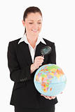 Beautiful female in suit holding a globe and using a magnifying 