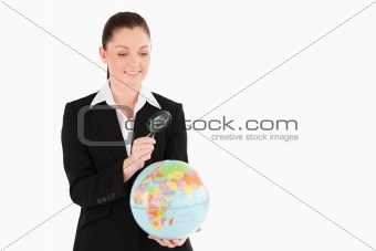 Cute female in suit holding a globe and using a magnifying glass