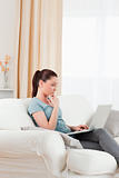 Pensive woman relaxing with her laptop while sitting on a sofa