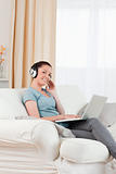 Charming woman with headphones relaxing with her laptop while si