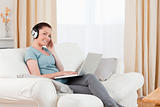 Pretty woman with headphones relaxing with her laptop while sitt
