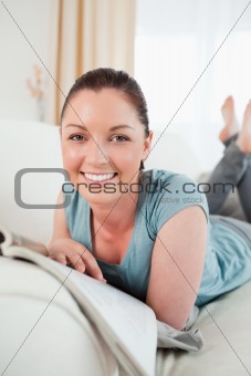 Cute woman reading a magazine while lying on a sofa