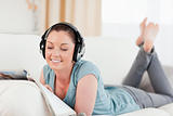 Lovely woman with headphones reading a magazine while lying on a