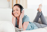 Charming woman with headphones posing while lying on a sofa