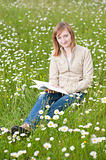 Beautiful young woman reading a book outdoors on a grass field i