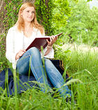 Beautiful young woman reading a book outdoors on a grass field i