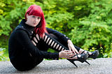 Sexy young girl with red hair in black dress rests in park