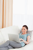 Cute woman relaxing with her laptop while lying on a sofa