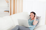 Gorgeous female with headphones relaxing on her laptop while lyi