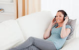 Good looking female using headphones while lying on a sofa