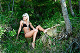 blonde girl in a black bathing suit sitting in the forest