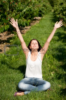 Cute young girl sitting on ground with hands up at cherry planta