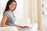 close up of a smiling woman sitting crossleged on sofa working w