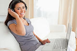 cute woman sitting on sofa with notebook and earphones looking i