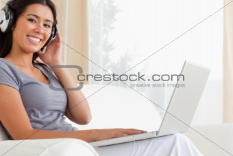 happy woman sitting on sofa with notebook and earphones looking 