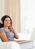 smiling woman sitting on sofa with notebook and earphones lookin