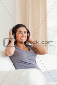 smiling woman sitting on sofa with earphones looking up