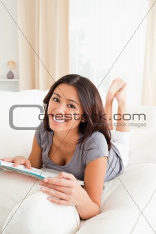 cute woman lying on sofa with magazine looking into camera