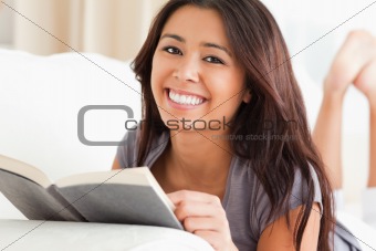 close up of a charming woman lying on sofa reading a book lookin