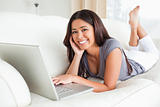 cute woman lying on sofa with notebook smiling into camera