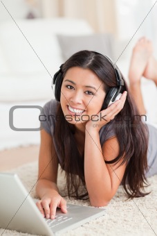 charming woman lying on a carpet with laptop and earphones looki