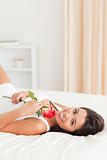 charming woman with rose lying on bed looking into camera