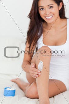 brunette woman putting cream on her legs smiling into camera