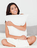 cute woman with pillow sitting on her bed smiling into camera