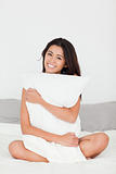smiling woman with pillow sitting on her bed looking into camera