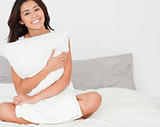 charming woman with pillow sitting on her bed looking into camer