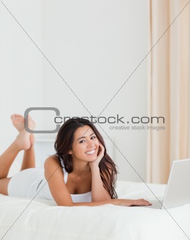 smiling woman lying on bed with crossed legs and laptop looking 