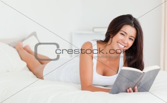 dark-haired woman lying on bed with book