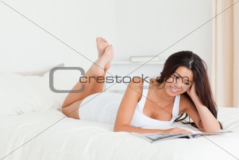charming woman lying on bed reading a magazine 