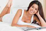 close up of a charming woman lying on bed reading a magazine loo