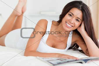 close up of a charming woman lying on bed reading a magazine loo