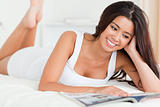 close up of a charming woman lying on bed reading a magazine