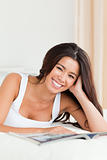 close up of a smiling woman lying on bed reading a magazine look