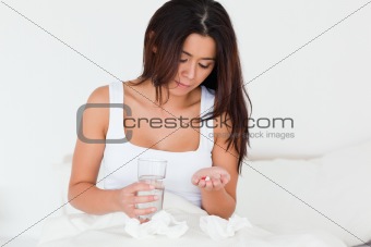 brunette woman having a cold sitting in bed taking pills
