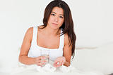 brunette woman having a cold sitting in bed taking pills looking