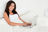 dark-haired woman with notebook lying in bed looking into camera