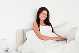 charming woman with notebook lying in bed looking into camera