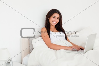 charming woman with notebook lying in bed looking into camera