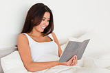smiling woman reading book lying in bed 
