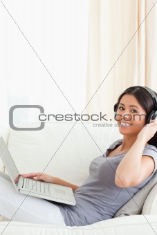 young woman looking into camera while sitting on sofa with earph