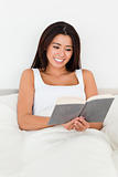 brunette woman reading book lyling in bed
