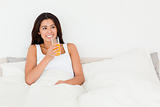 dark-haired woman dinking orange juice sitting in bed looking at