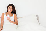 smiling woman holding orange juice sitting in bed looking into c