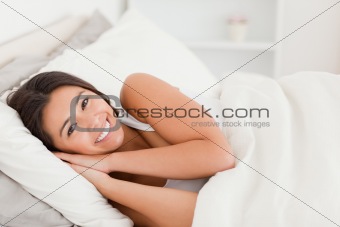 close up of a smiling dark-haired woman lying under sheet